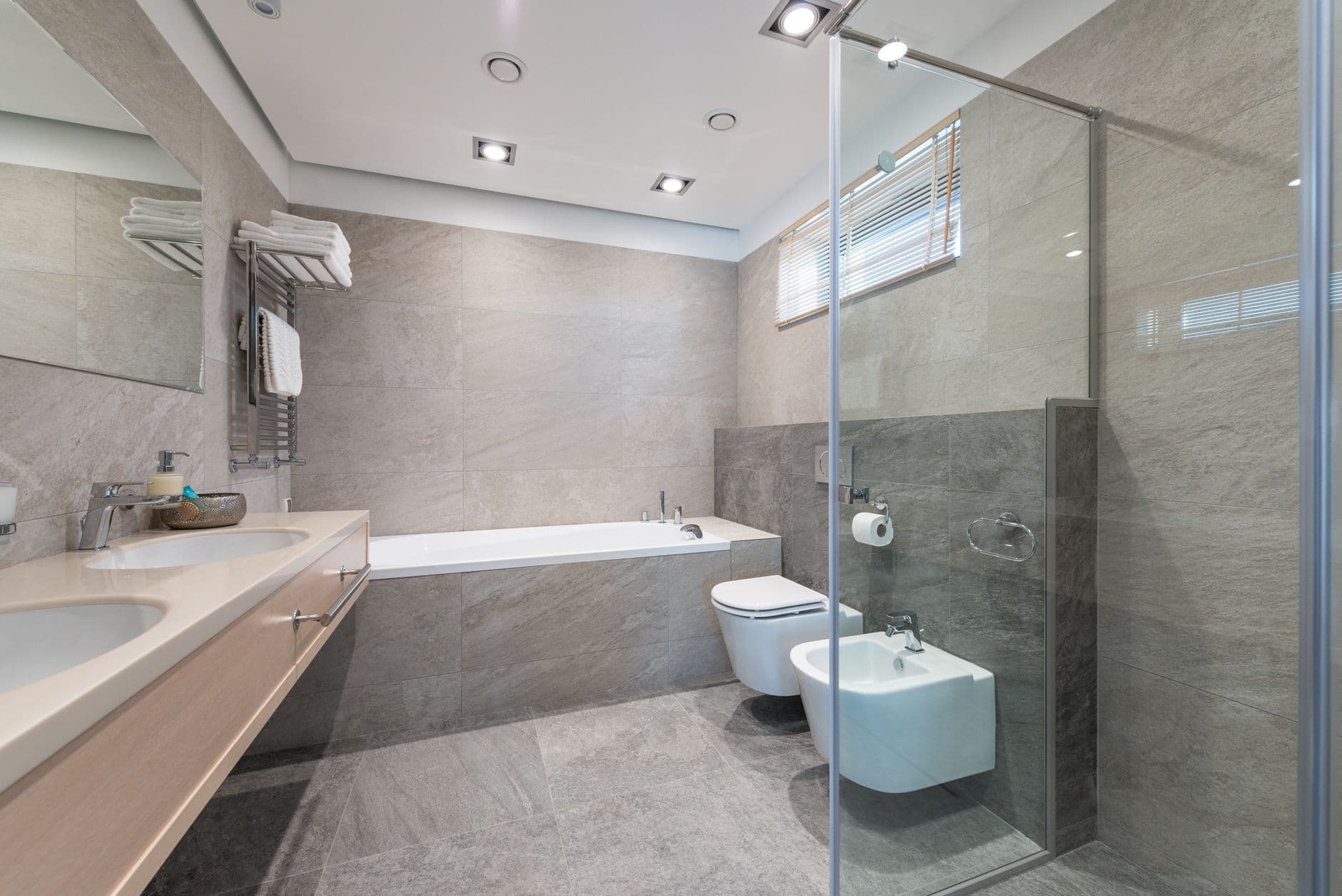 Bathroom lined in one pale stone with integrated basins and a restrained joint pattern