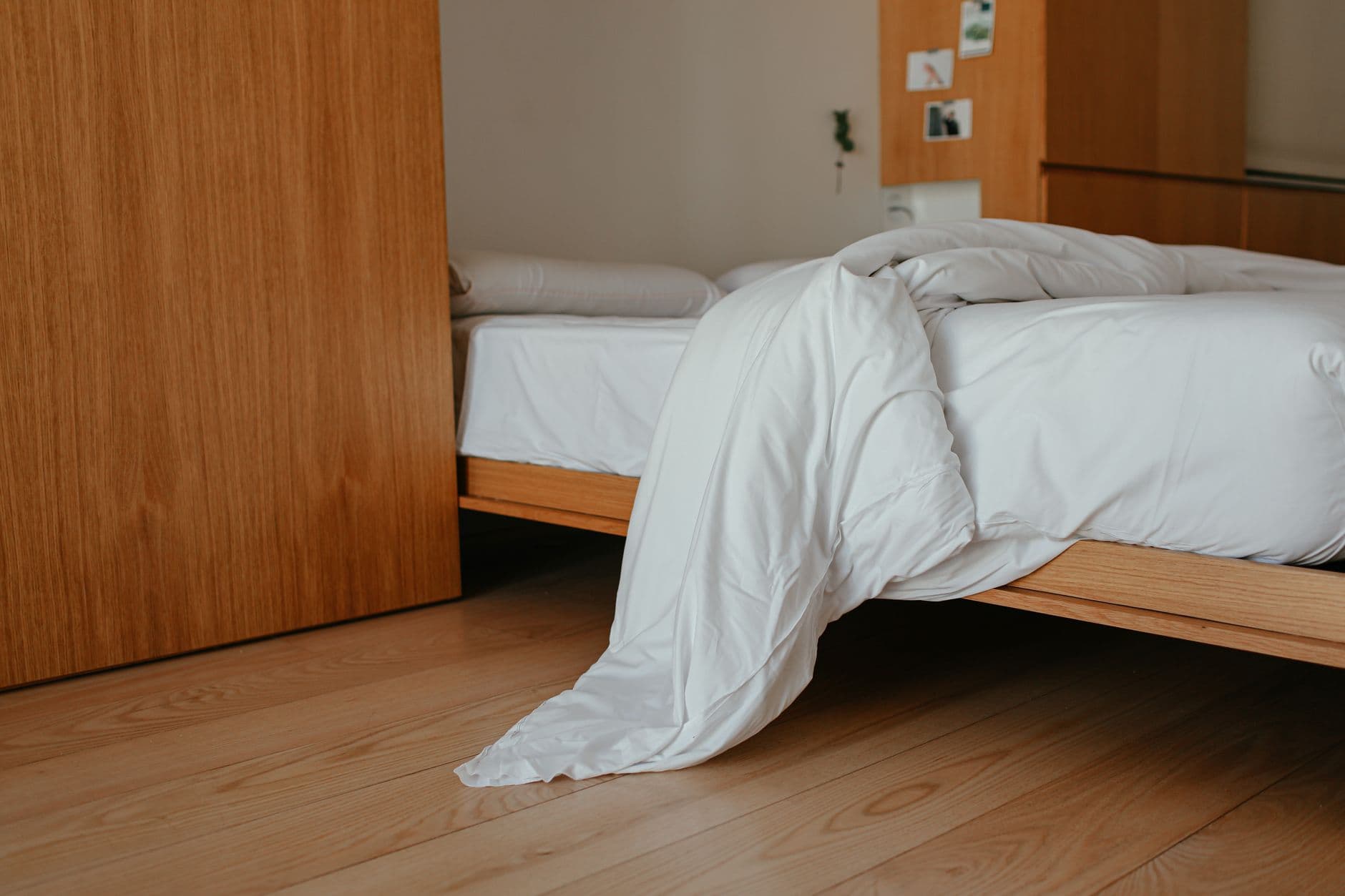Low timber platform bed with loose neutral bedding and visible floor around the frame