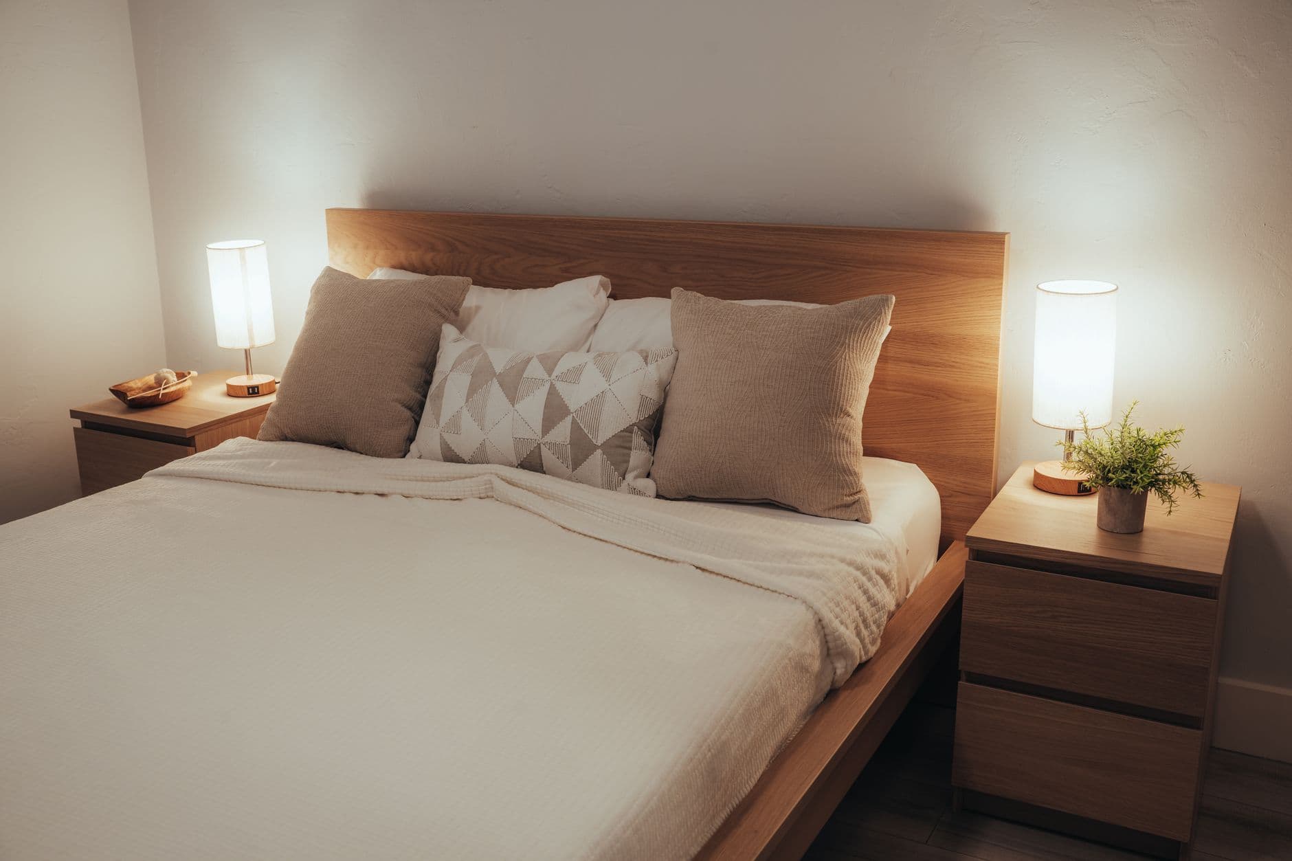 Simple round timber nightstand with one shaded lamp beside a neatly made bed