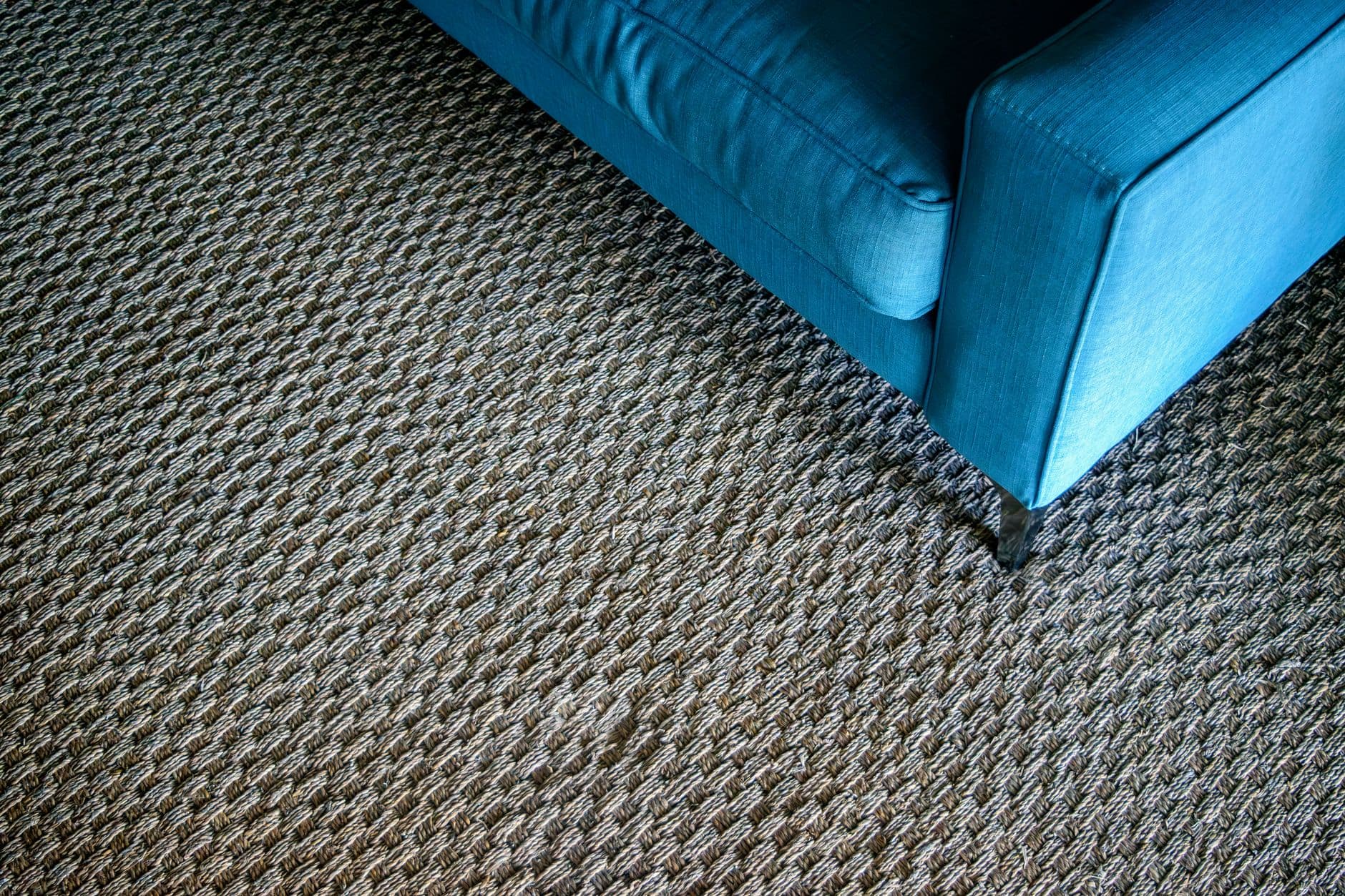 Blue upholstered sofa standing on a textured woven carpet in a bright room