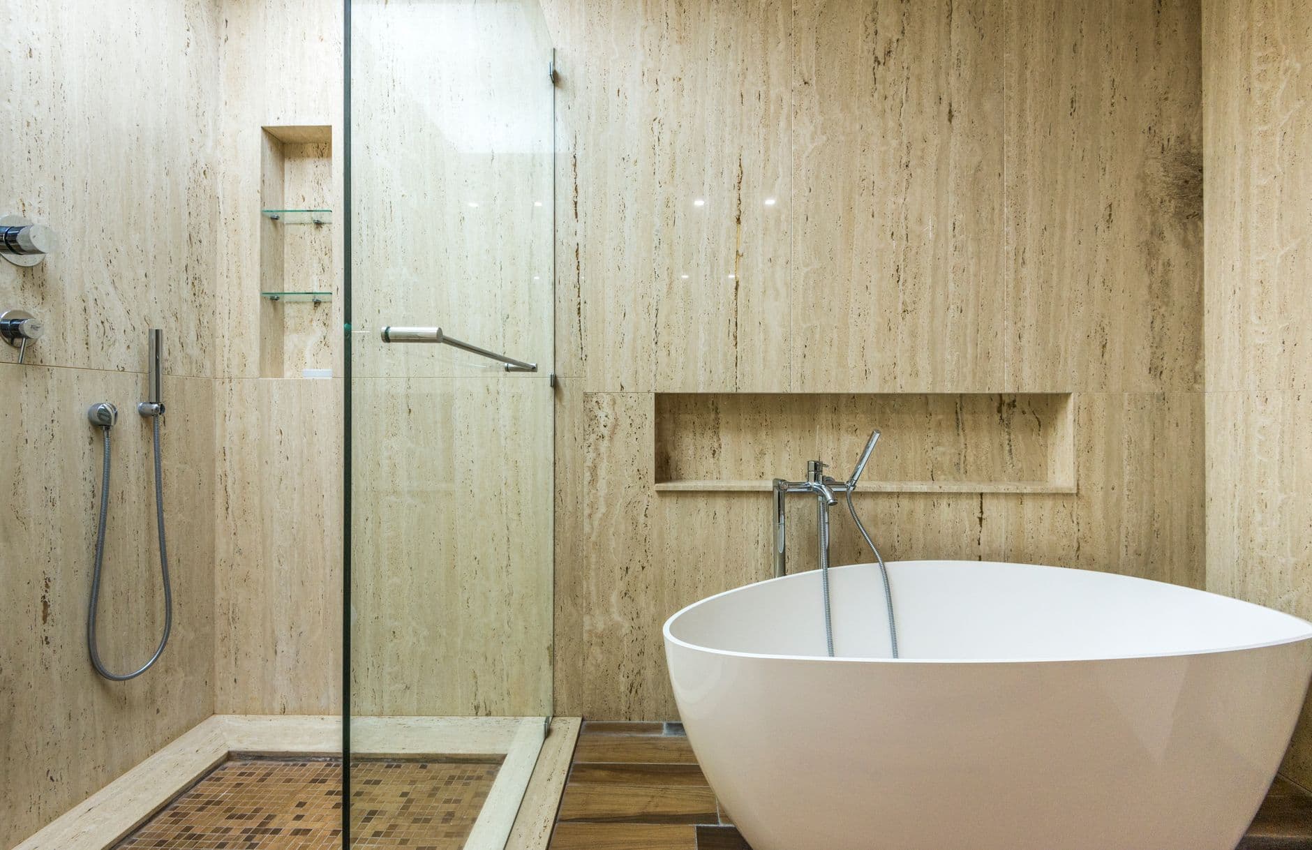 Freestanding white bath set against pale travertine walls and a glazed shower