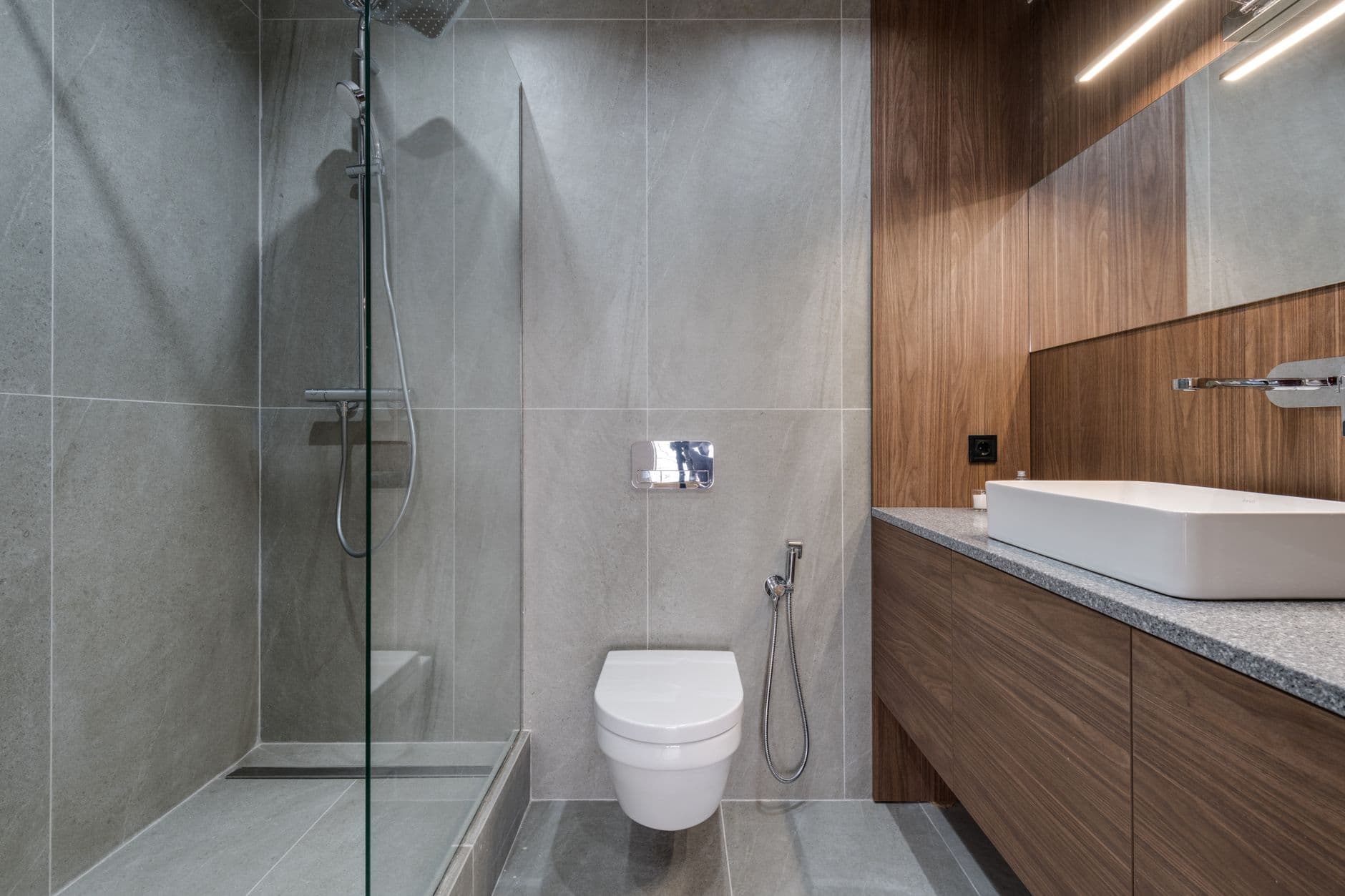 Open walk-in shower with a continuous pale stone floor and frameless glass