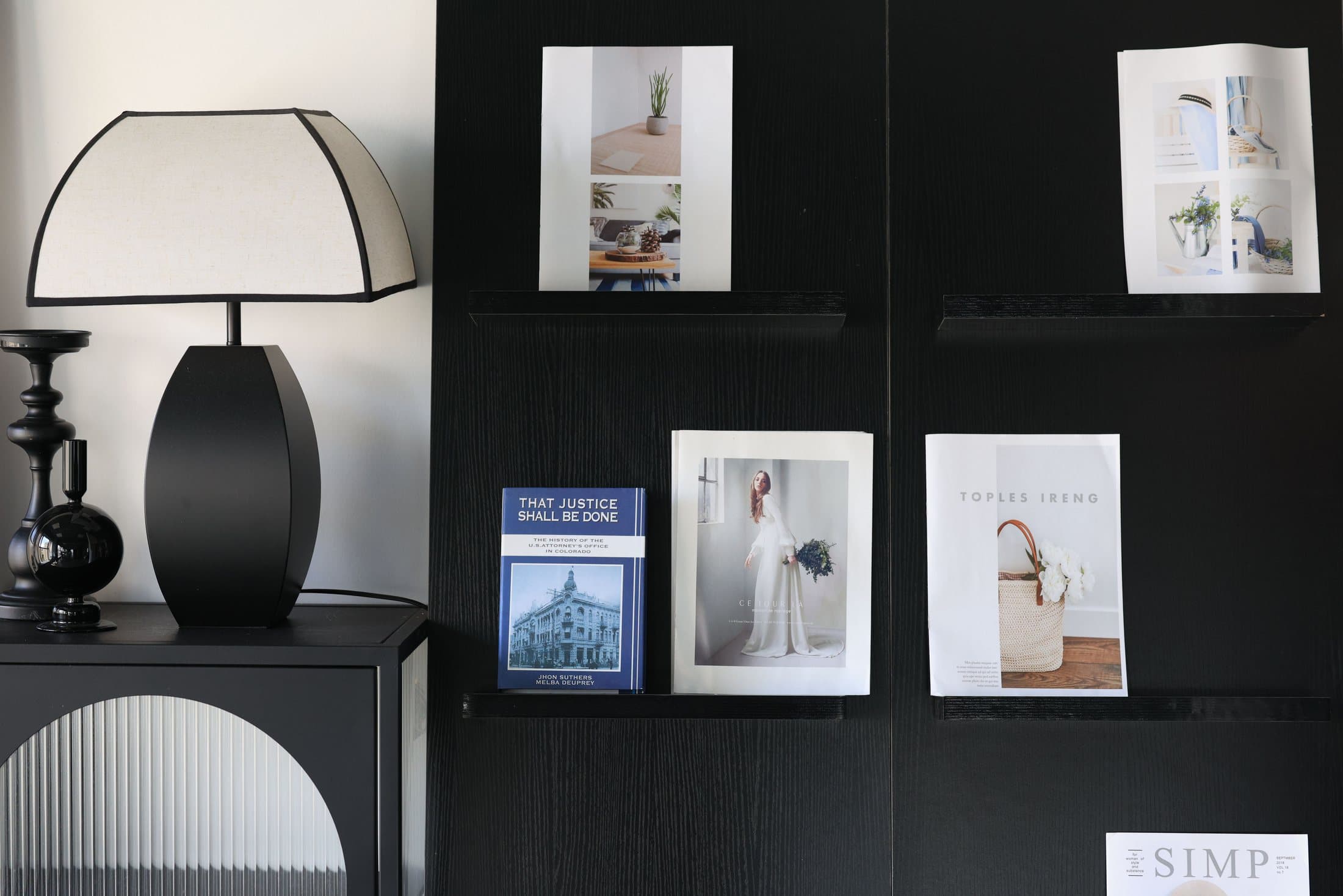 Black wall-mounted bookshelf with magazines, books and a table lamp