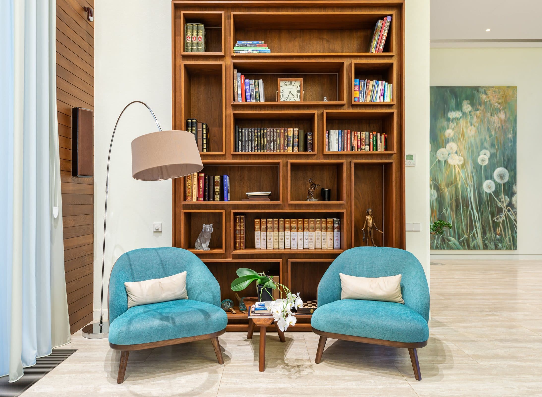 Living room with blue armchairs and a full-height wooden bookcase
