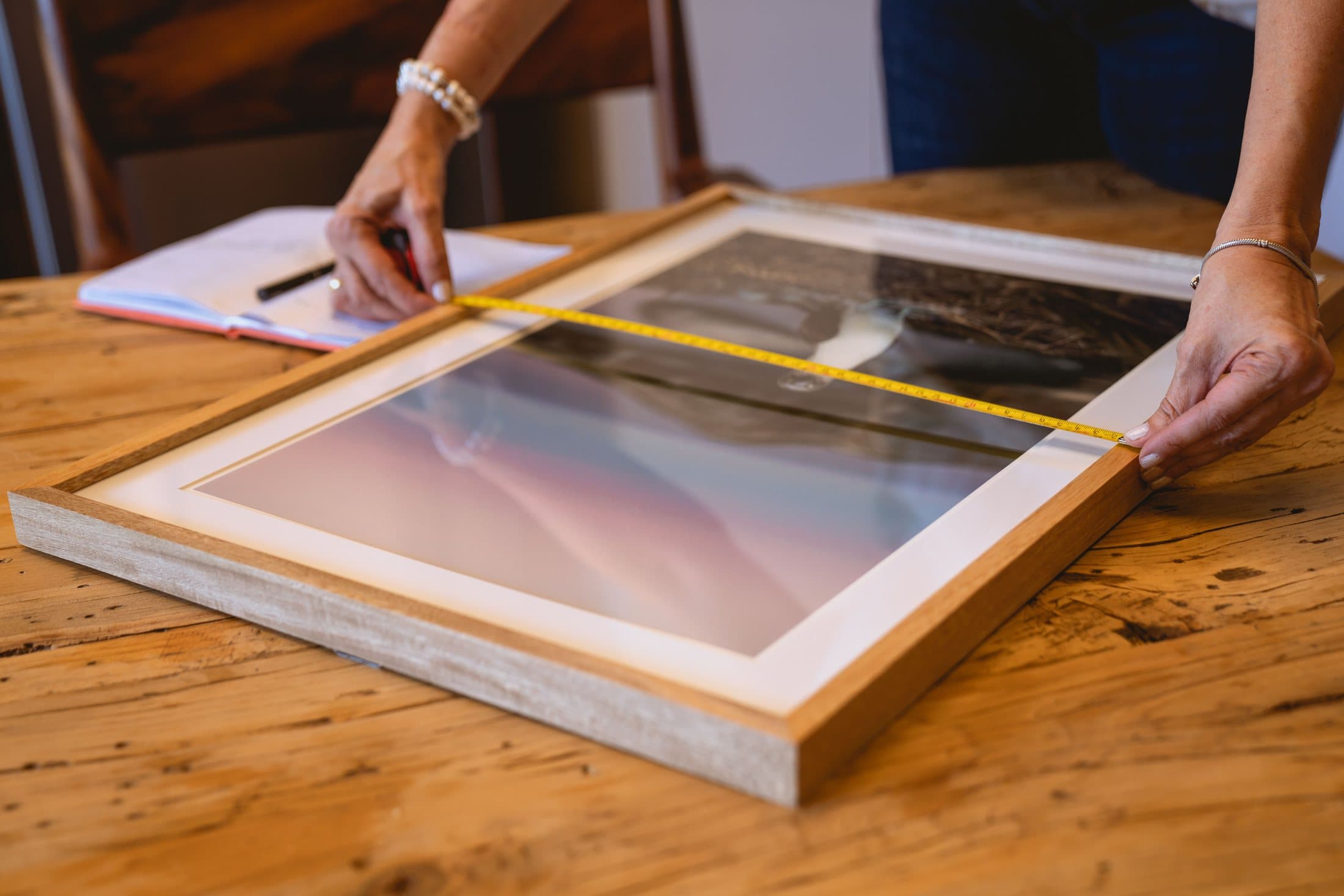 Hands measuring a wooden picture frame before hanging it