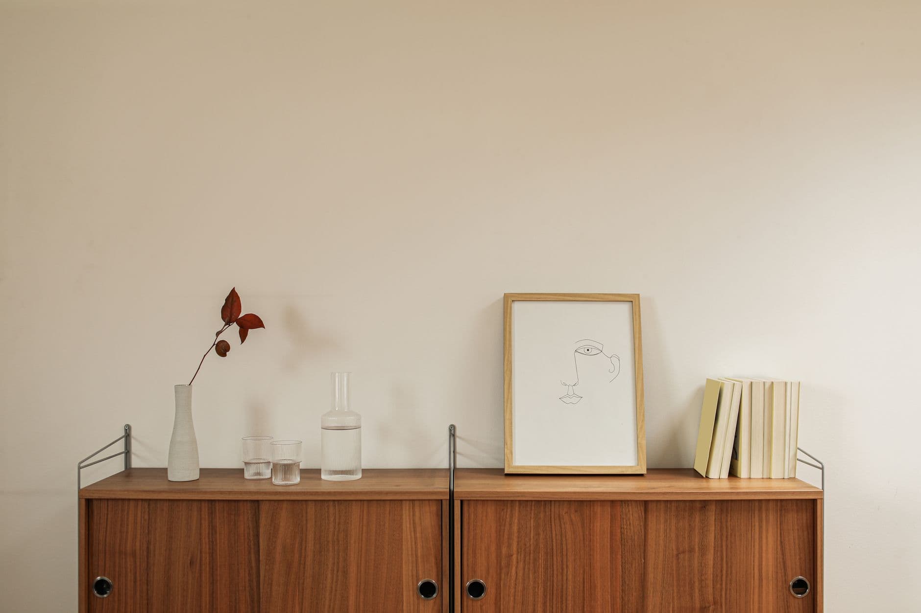 Shelf with a framed print, book and a few glass objects arranged with open space